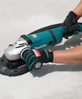 Person using Makita grinder with 7 Inch Dust Extraction Surface Grinding Shroud With Soft Brushes And Four Spring Suspension Keeps It Flush During Use Removable Edge Piece For Flush Surfaces Standard Hose Fitting Fits Most Vacs on concrete