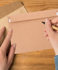 A4 Self Sealing Kraft Brown Envelopes Pack Of 30 Thickened Flat Cardboard Mailers being handwritten on a wooden table