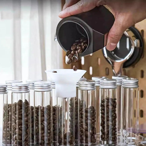 Pouring coffee beans into clear glass canisters of the 14 Piece Single Dose Coffee Bean Storage Tubes With Airtight One Way Valve.