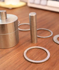 Coin Ring Puncher And Spacer Set For Jewelry Making With Six Spacer Rings showing metal puncher and rings on a wooden surface.