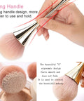 Hand holding large nail dust brush cleaner, long gold handle with pink nylon bristles. 2 Pack Nail Dust Brush Cleaners For Acrylic Dip Powder Makeup And Blush Large Manicure Cleanup Tools For Salon And Home Use Nail Art Gold And Black Kit.