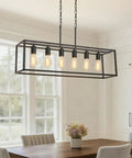 Slick Black 6 Light Linear Chandelier above dining table, matte steel frame, adjustable mount, modern farmhouse style.