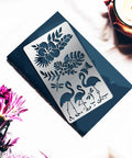 Heavy Duty Metal Flamingo And Butterfly Cutting Template Four By Seven Inches Reusable Patterns For Card Making Wood Burning Leather Crafting Spray Painting Badass Craft Gear on a dark surface with flowers.