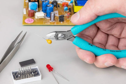 Close-up of Four And A Quarter Inch Magic Diagonal Small Head Cutter cutting a wire with PCB components, blue and silver finish, Swiss made.