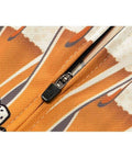 Close-up of orange and black zipper detail on fabric with dice pattern.