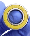 Close-up of a Stainless Steel Ceramic Hybrid Radial Bearing For Bike Hubs 15x28x7mm ABEC3, with yellow seal and marking SC6902RS
