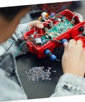 Person using 100Pcs Eyeglass Repair Screws Kit For Quick Eyewear Fixes, with screws and electronic wires visible on table.