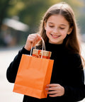 Girl holding orange bag from Small Kraft Gift Bags With Handles Set Of 32 In Rainbow Colors Five Point Eight By Three Point Two By Eight Point Two Five Inches Eco Friendly Party Favor Bags For Kids Birthday Baby Shower Weddings Crafts And Party Supplies
