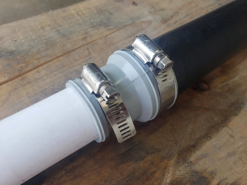 Flexible DWV Reducing Coupling 1-1/2 Inch To 1-1/4 Inch Drain Waste Vent Piping Connector With Easy Push In Installation DIY Friendly For In Home Repairs Cut Ins And House To Main Lines Durable Plumbing Fit, shown clamped to white PVC pipe