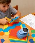 Child using Two And A Half Inch Circle Hole Punch Cutter for paper crafts on colored sheets at a desk.