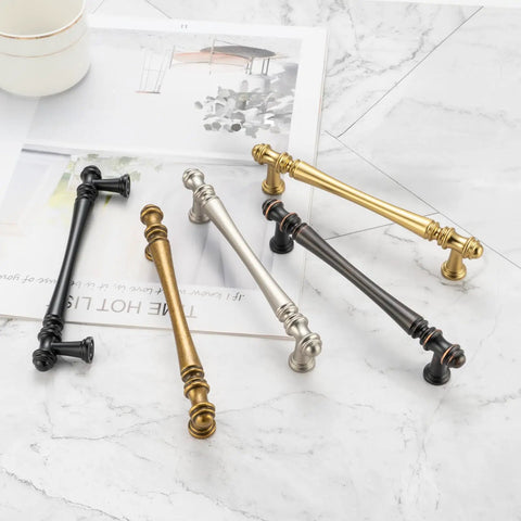 Assorted metal cabinet handles on marble surface showcasing vintage, brass, bronze, and black finishes.