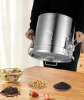 Heavy Duty 304 Stainless Steel Airtight Food Storage Canister With Snap Tight Buckle Closure Perfect For Rice Flour Grains And Coffee Beans Massive Twenty Six Gallon Bucket being held above ingredients on a wooden table.