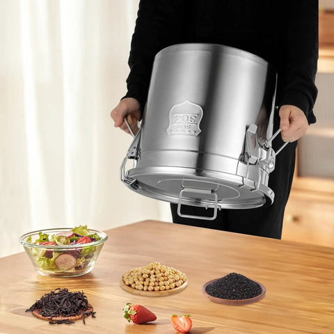 Heavy Duty 304 Stainless Steel Airtight Food Storage Canister With Snap Tight Buckle Closure Perfect For Rice Flour Grains And Coffee Beans Massive Twenty Six Gallon Bucket being held above ingredients on a wooden table.
