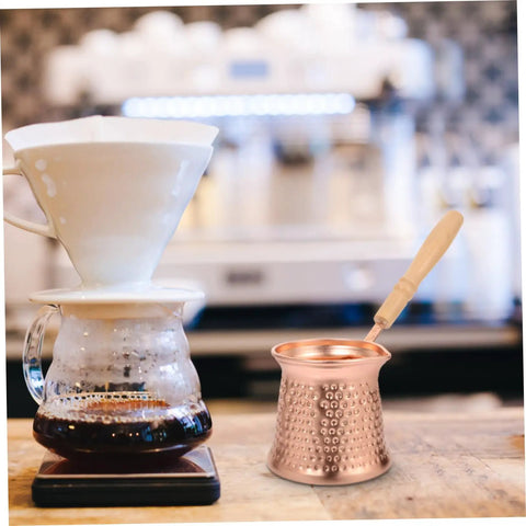 Copper Turkish Coffee Pot With Wooden Handle For Quick Brew And Multi Purpose Beverage Kettle No Fuss Pour For Traditional Arab Cezve On Induction Stovetops displayed on a counter next to a coffee dripper on a glass carafe.