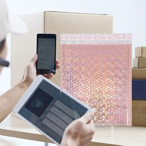 Person using mobile devices next to Rose Pink Holographic Padded Mailers 25x30cm Self Seal Waterproof Shipping Bags 10 Pack for mailing