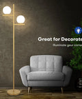 2 Globe Modern Floor Lamp With Foot Pedal Frosted Glass Shades Brass Gold Finish next to gray armchair in living room.