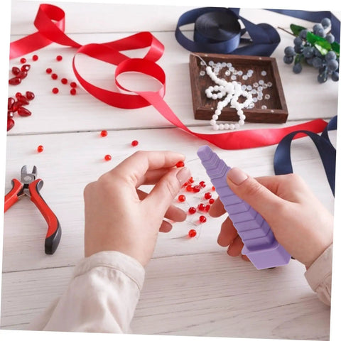 Hands holding a mandrel from the 4 Piece Plastic Mandrel Set For Jewelry Making, next to red beads and jewelry tools on a table.