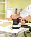 Multi-Jetstream Dust-Free Random Orbital Finish Sander operating on a wood panel with variable speed and soft start features.