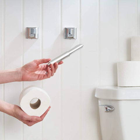Spring Loaded Toilet Paper Roll Holder Replacement in chrome finish being installed in a bathroom with white walls and stacked toilet paper rolls.