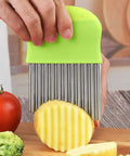 Crinkle cutter knife with green silicone handle and stainless steel blades slicing a potato.