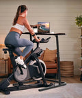 Woman using bike trainer with adjustable treadmill desk for home office in living room setting.