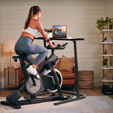Woman using bike trainer with adjustable treadmill desk for home office in living room setting.