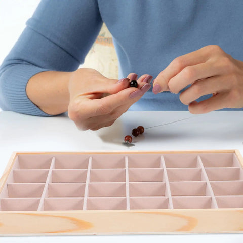 Person threading beads in Straight Up Premium Pine Wood Jewelry Tray With 24 Compartments And Plush Velvet Lining To Store Your Bling.