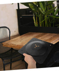Heavy Duty Cast Iron Coffee Table Leg Connector Plate With Rock Solid Mounting Screws held above a wooden table, black finish visible.