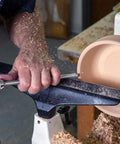Side view of a mid-size carbide woodturning tool with charcoal translucent handle shaping a wooden bowl on a lathe.