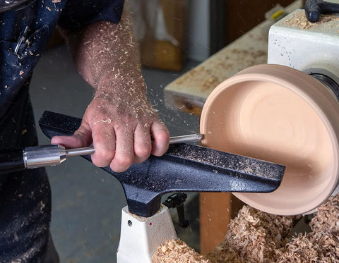 Side view of a mid-size carbide woodturning tool with charcoal translucent handle shaping a wooden bowl on a lathe.