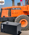 10 Gallon Welded Steel Hydraulic Reservoir Tank 14 Gauge Metal Construction Black Finish With 2 Inch Suction Port And 0.75 Inch Return Port For Reliable Fluid Storage And Smooth Pump Operation shown in front of an orange construction vehicle.