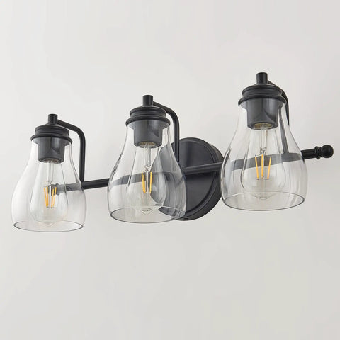 Black Three Light Vanity Light Fixture With Clear Glass Shades For Bathroom Over Mirror, shown mounted on a white wall.