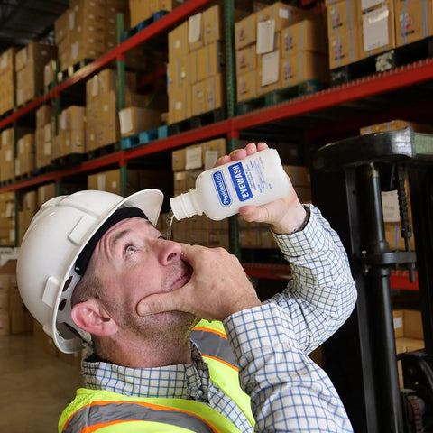 PhysiciansCare Eye Wash Solution, 16-oz white bottle with blue label, used to flush an eye in a warehouse.