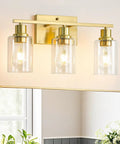 Three-Light Vanity Light With Clear Glass Shades In Brushed Brass Finish Wall Sconce Above Bathroom Mirror