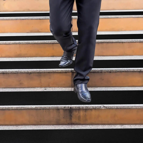 Person walking down stairs with Heavy-Duty Anti-Slip Tape 18 In By 40 Ft For Indoor Outdoor Use On Ramps Stairs Garage Floors Warehouses And Workshops Black Abrasive Non-Slip Grip Roll applied on steps.