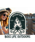 Person wearing hat and sunglasses outdoors beside a 'Boss Life Outdoors' logo with campfire illustration