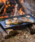 Cooking fish with lemons on a seasoned carbon steel griddle with dual-handle flat top over campfire, 18 by 10 inches.