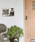 Train Station Steam Locomotive Metal Sign 8x12 Inch Vintage Retro Wall Decor on white wall near wicker chair, door, plant