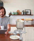 No Sweat Heavy Duty Cast Iron Grain Mill Featuring Wooden Hand Crank And Secure Table Clamp For Grinding Corn Wheat Oats Into Home Pantry Fresh Flour with flour bowl.