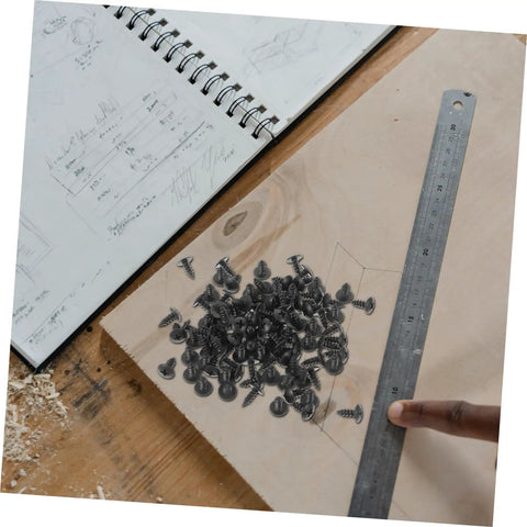 Miniature Metal Screws Set Of 100 Self Tapping Mounting Fasteners For Furniture Repair And DIY Projects laid on wood with notebook and ruler
