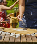 Person sprinkling flour on a Heavy Duty 14 Inch Bamboo Pizza Peel And Wooden Spatula Paddle For Backyard Cookouts.