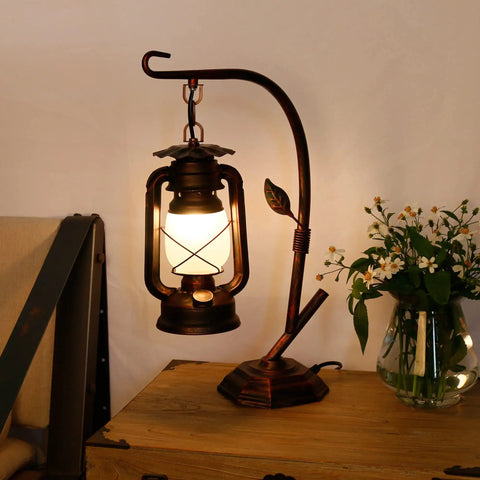 Rustic Lantern Table Lamp With Glass Shade For Living Room And Bedroom Cozy Nightstand Lighting For End Tables Farmhouse Style Bedside Lamp That Delivers Warm Homey Vibe, vintage metal design on wooden table next to flowers.