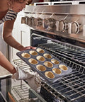 Person placing muffin tray in oven, not related to Microwave Crisper Pan Replacement Universal Metal Fry Pan For Even Browning OEM-Grade.