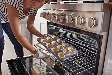 Person placing muffin tray in oven, not related to Microwave Crisper Pan Replacement Universal Metal Fry Pan For Even Browning OEM-Grade.