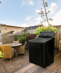 Front view of a black fabric washer and dryer cover on an outdoor wooden deck