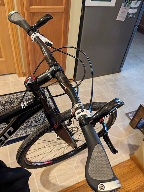 Close-up of Dope Carbon Mountain Bike Bar Ends 22.2mm Ergonomic Handlebar Ends For MTB on black bike in home setting
