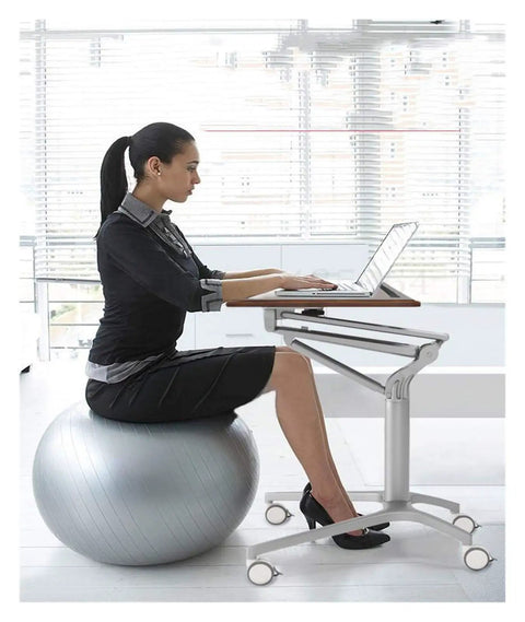 Adjustable Mobile Overbed Table Featuring Smooth Rollin Casters And Beastly Stable Base used as a laptop desk beside a ball chair.