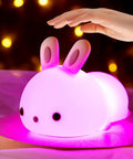 Lit Cute Bunny Night Light For Kids With 16 Colors Tap Control Dimmable Lamp on purple surface, hand reaching to tap