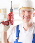 Front view of a worker holding a red cordless drill with a bit, wearing white helmet and safety glasses