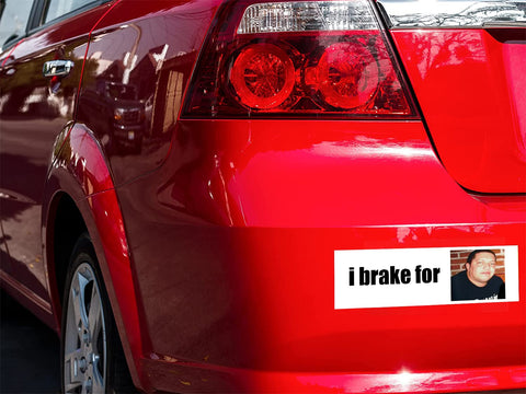 Rear bumper sticker on a red car; white decal reads i brake for with a small photo.